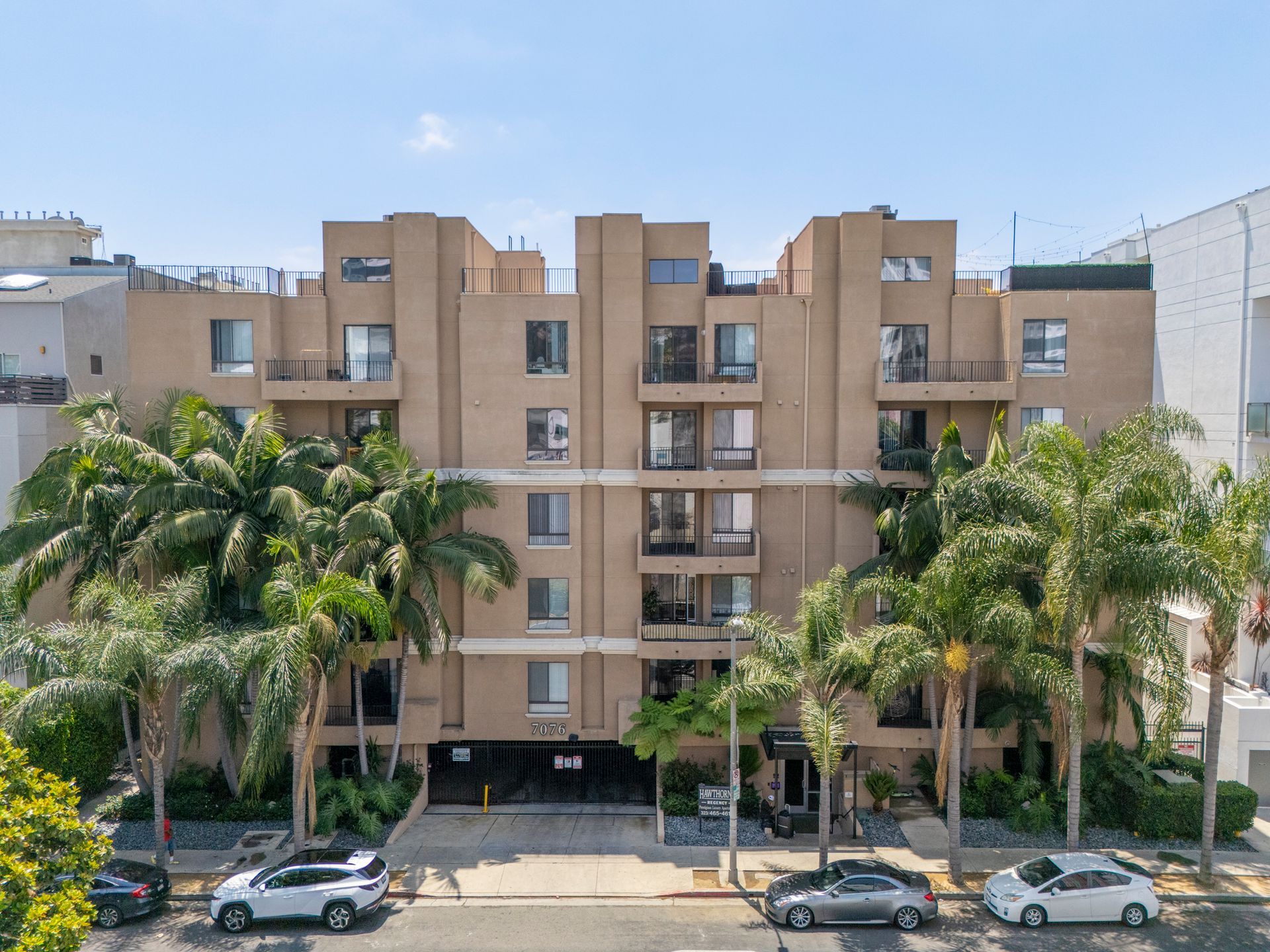 Apartment building with tan balconies and palm trees lining the street in front.