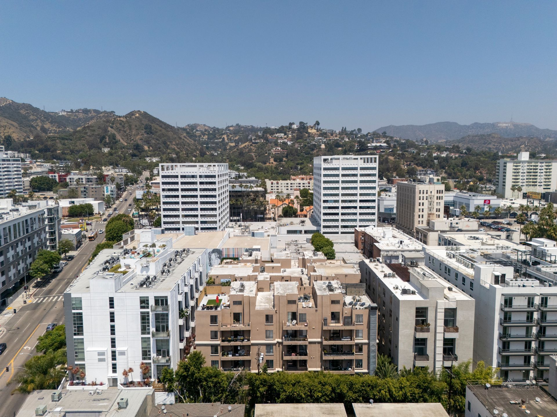 Aerial view of a sunny city block with modern apartment buildings and hills in the background
