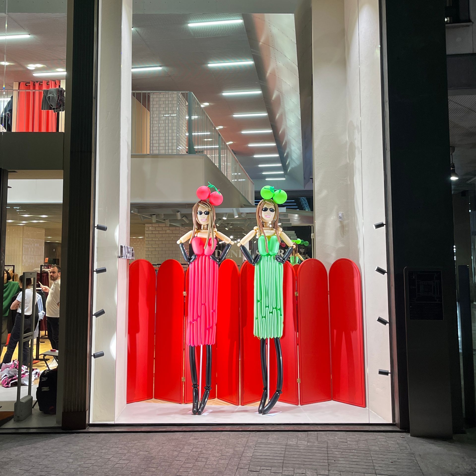 Two mannequins are standing in front of a red screen in a store window