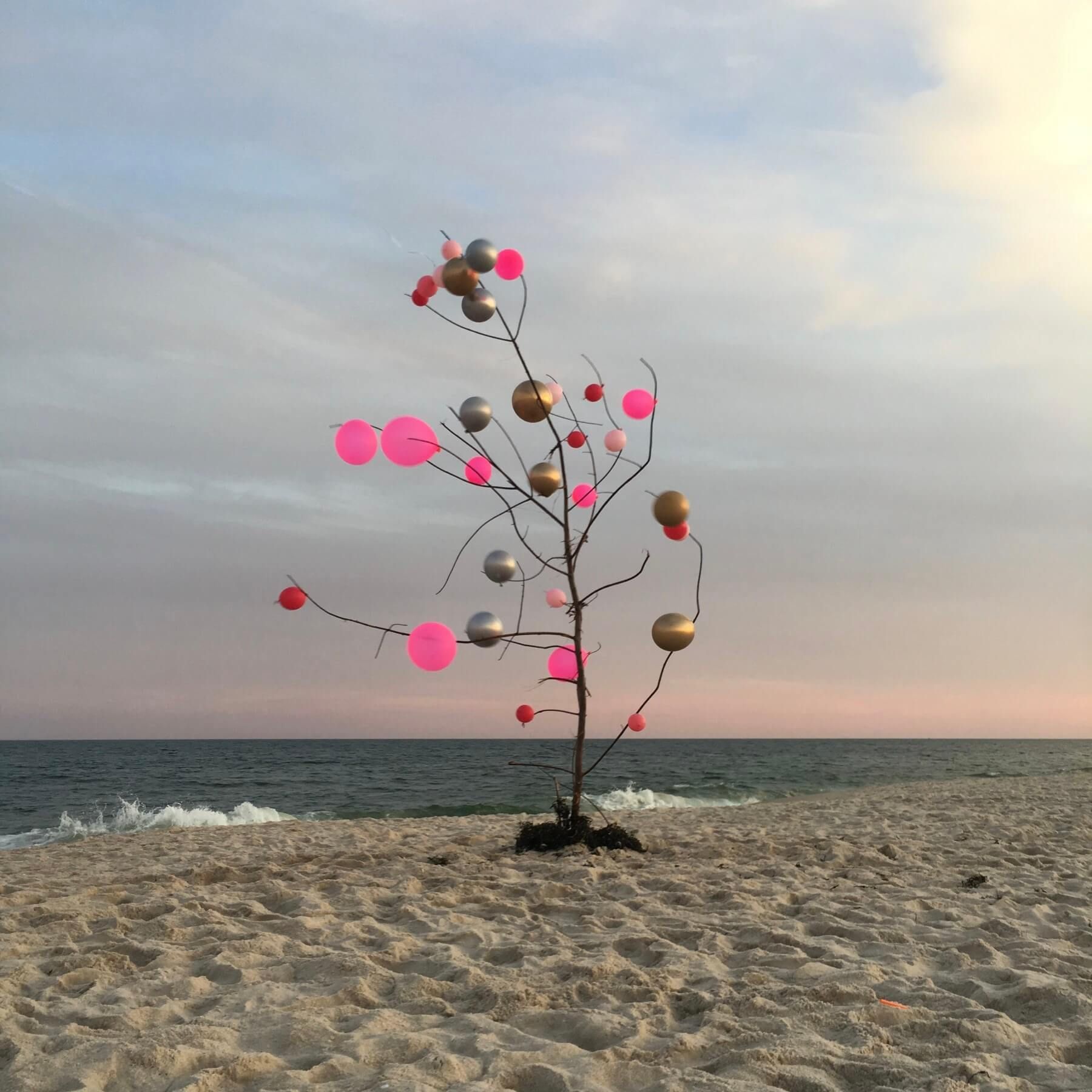 A tree with balloons on it is on the beach near the ocean