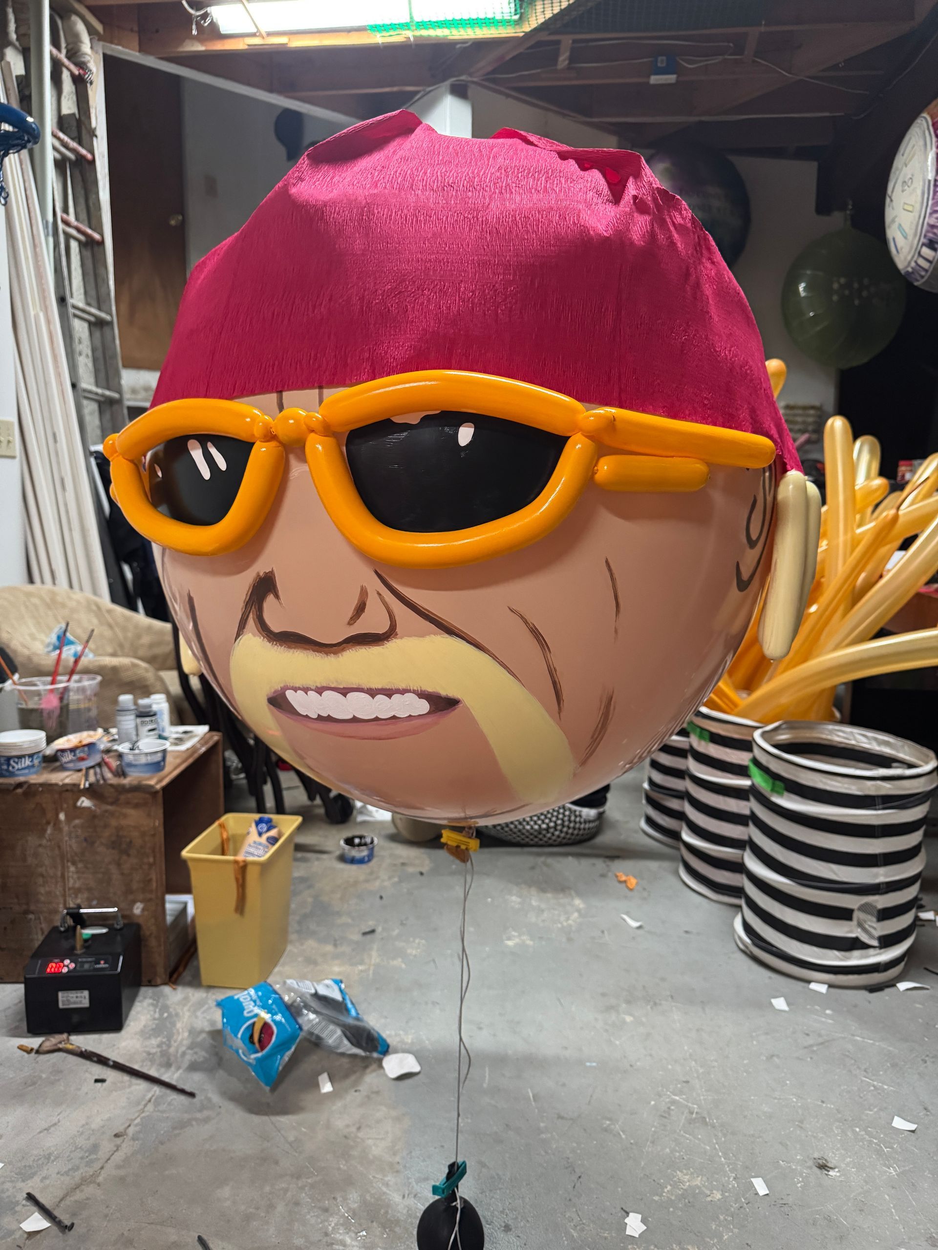 Large balloon decoration of a man with orange sunglasses, a red bandana, and balloon-made sideburns and fries.