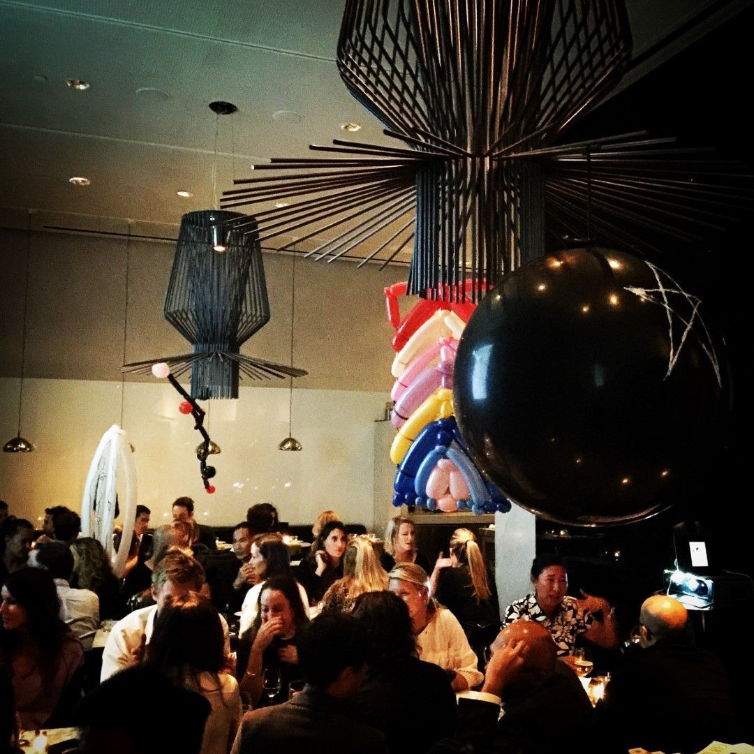 Restaurant interior with crowd, balloon decorations, unique light fixtures.