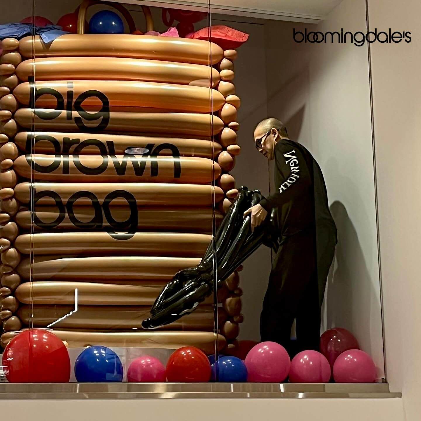 A man is standing in front of a big brown bag made of balloons