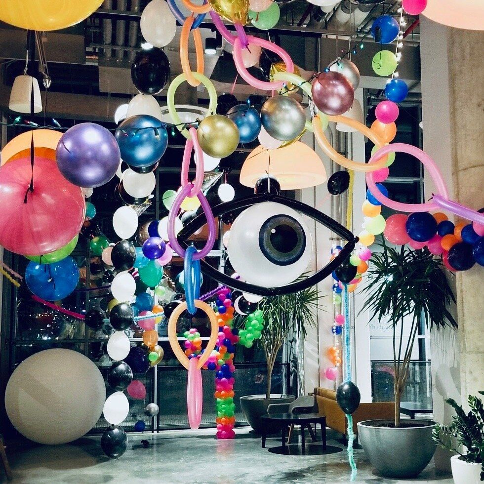 Colorful balloons, chains, and an eye art piece decorate a lobby area.