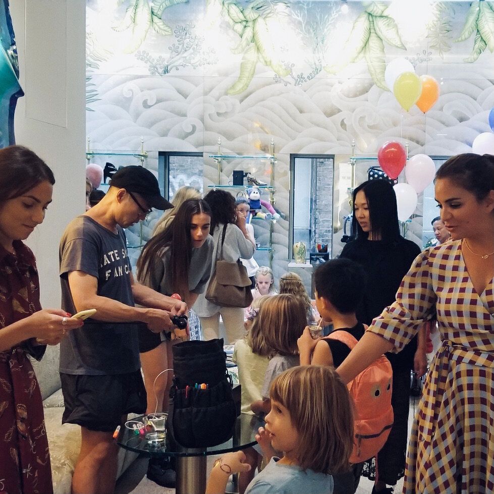 People inside a shop, balloons, children looking at something.