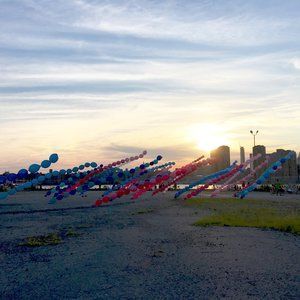 Blue and red balloons float over a city skyline at sunset.