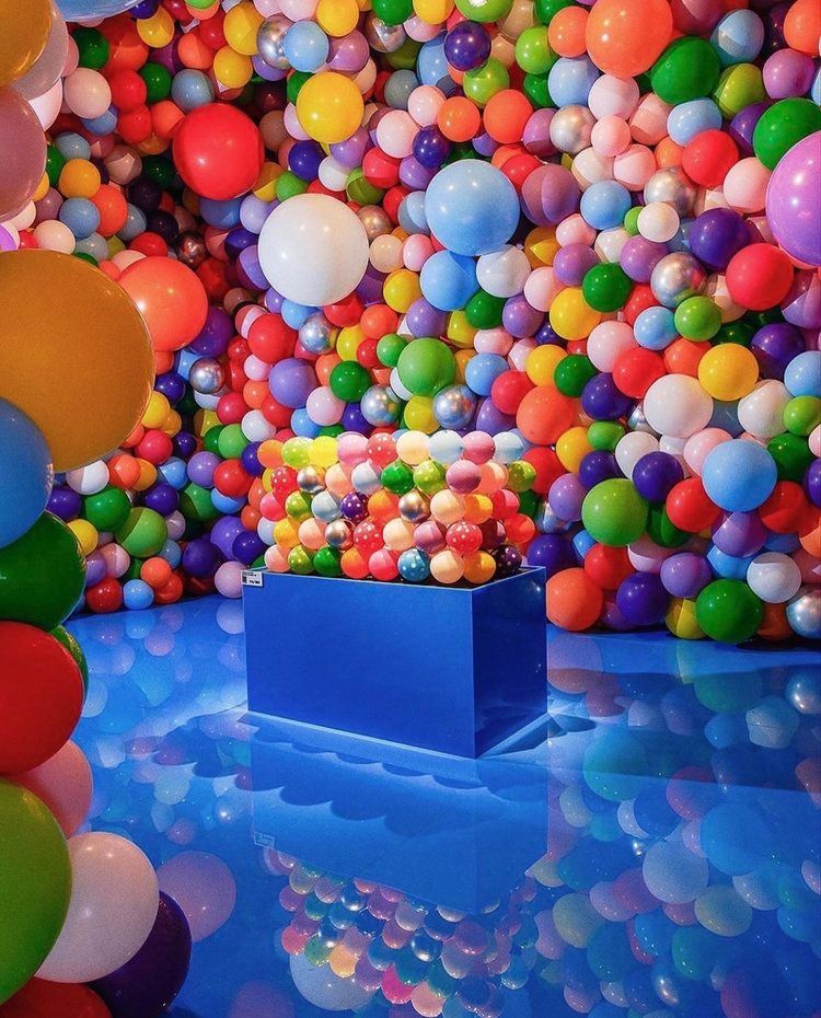 Room filled with colorful balloons; blue reflective floor and stand with more balloons.