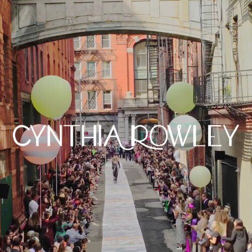 Cynthia Rowley fashion show in a narrow alley, models walking a runway, crowds on either side, balloons overhead.