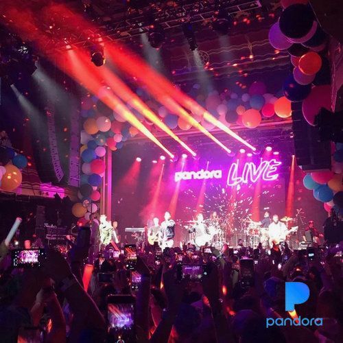 Band performing on stage at a Pandora LIVE concert, bright lights, crowd with phones raised, balloons.