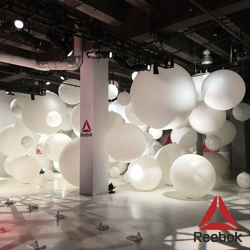 Reebok event with white spheres. A logo is in the bottom right corner of a large room.