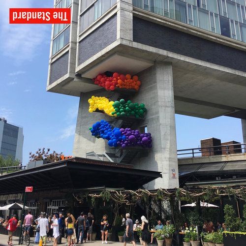 Rainbow balloons adorn The Standard hotel's pillars; people gather below, outdoor seating visible.
