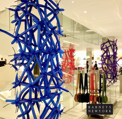 Blue, red, and purple balloon sculptures in a Barneys New York window display, with handbags below.