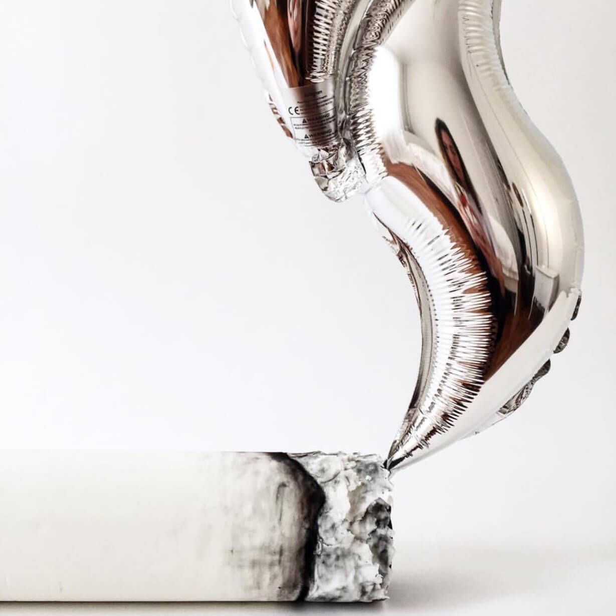 A silver balloon in the shape of a heart is sitting on a rock