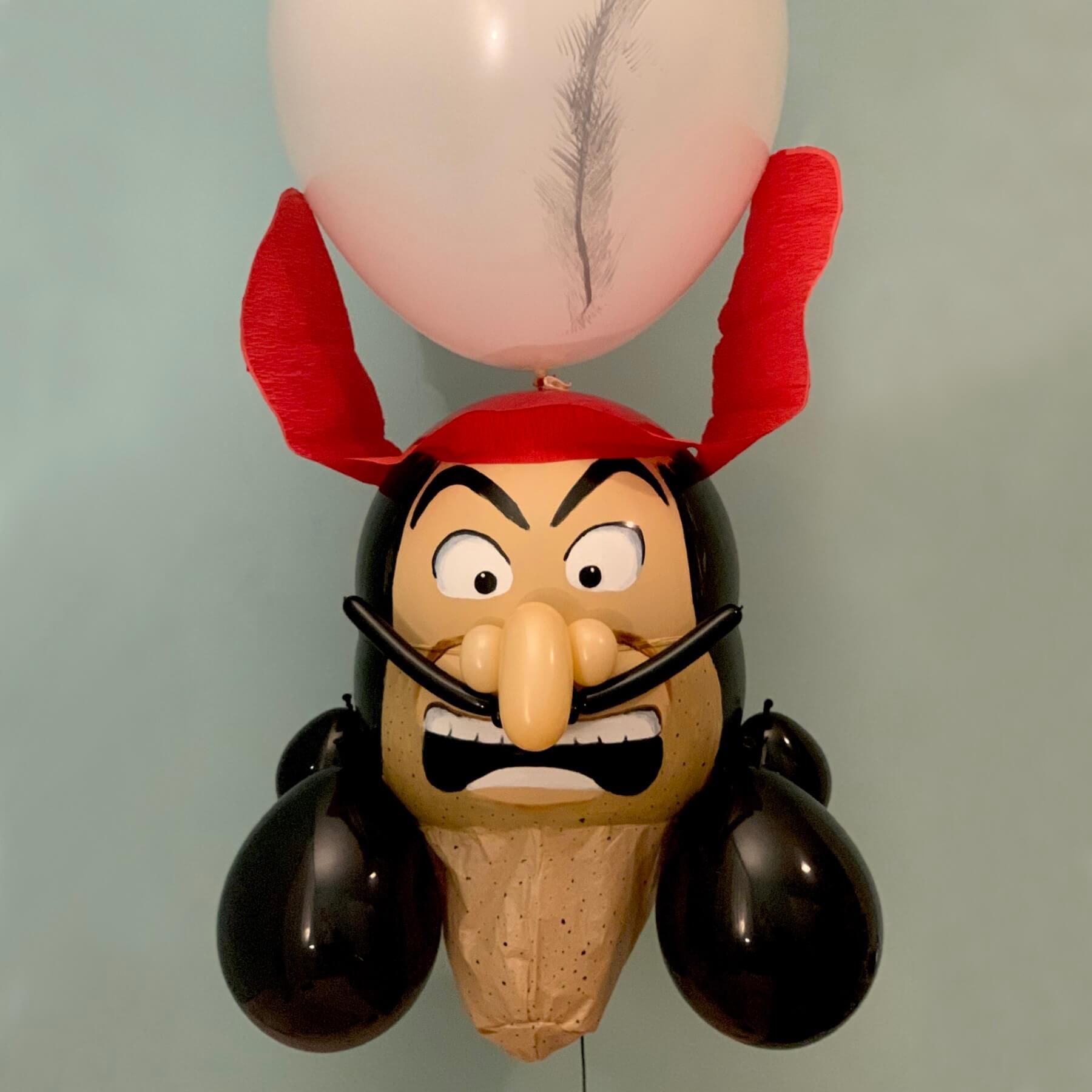 Balloon sculpture of a mustached villain with a red hat and a white balloon above his head.