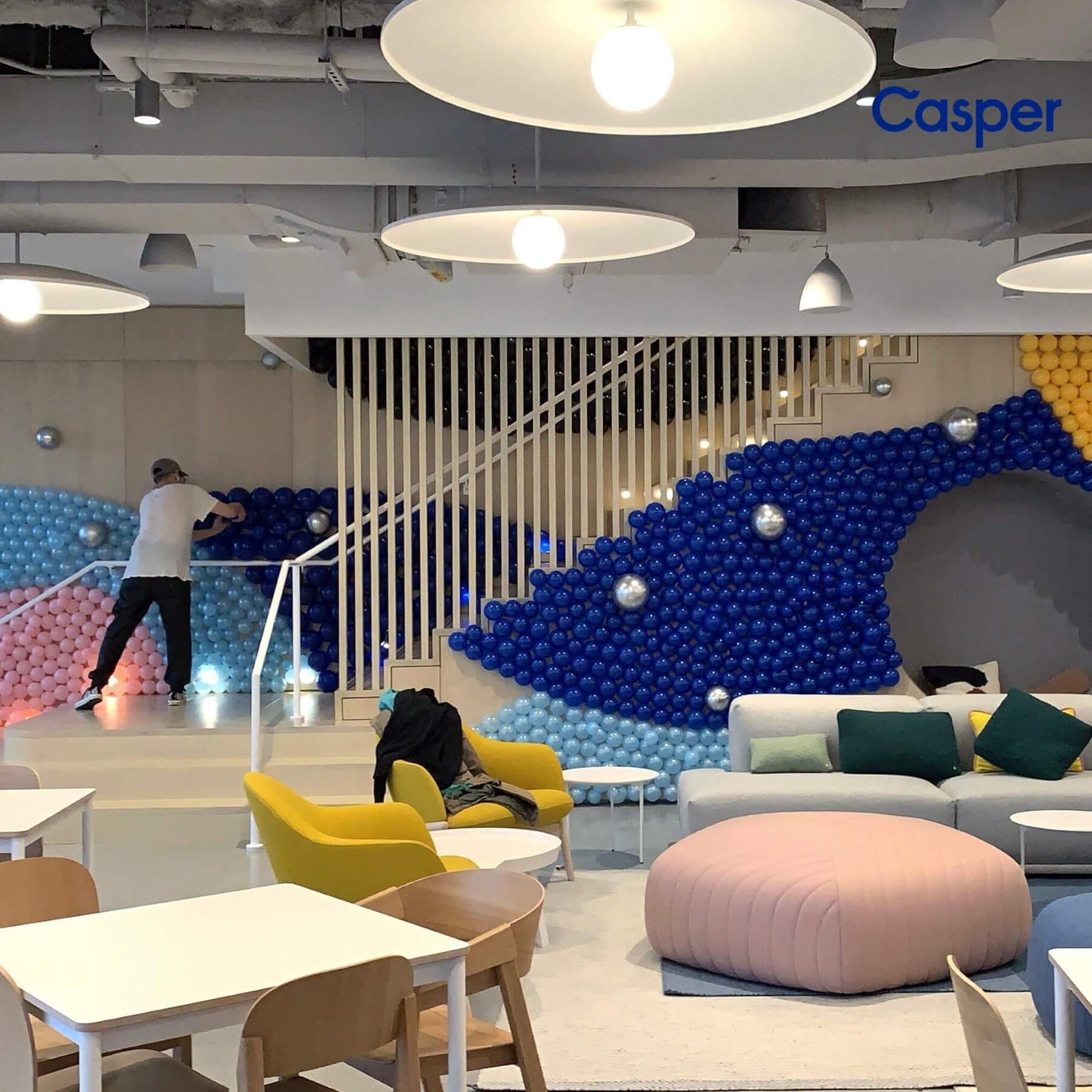 Playroom with blue ball pit staircase, seating, tables, and a person tossing balls.