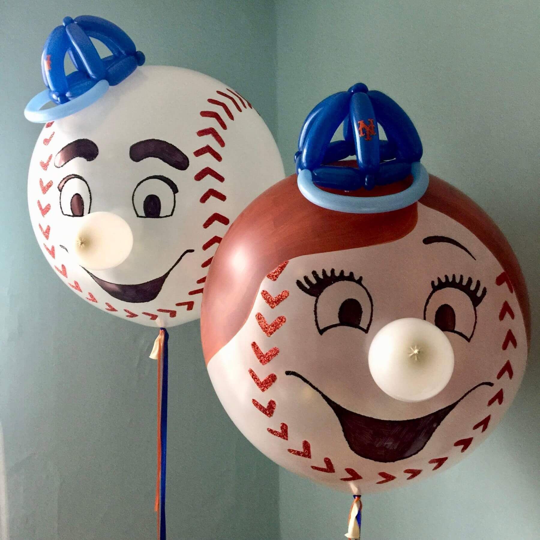 Two baseball-themed balloons with cartoon faces, hats, and nose attachments; one white, one brown.