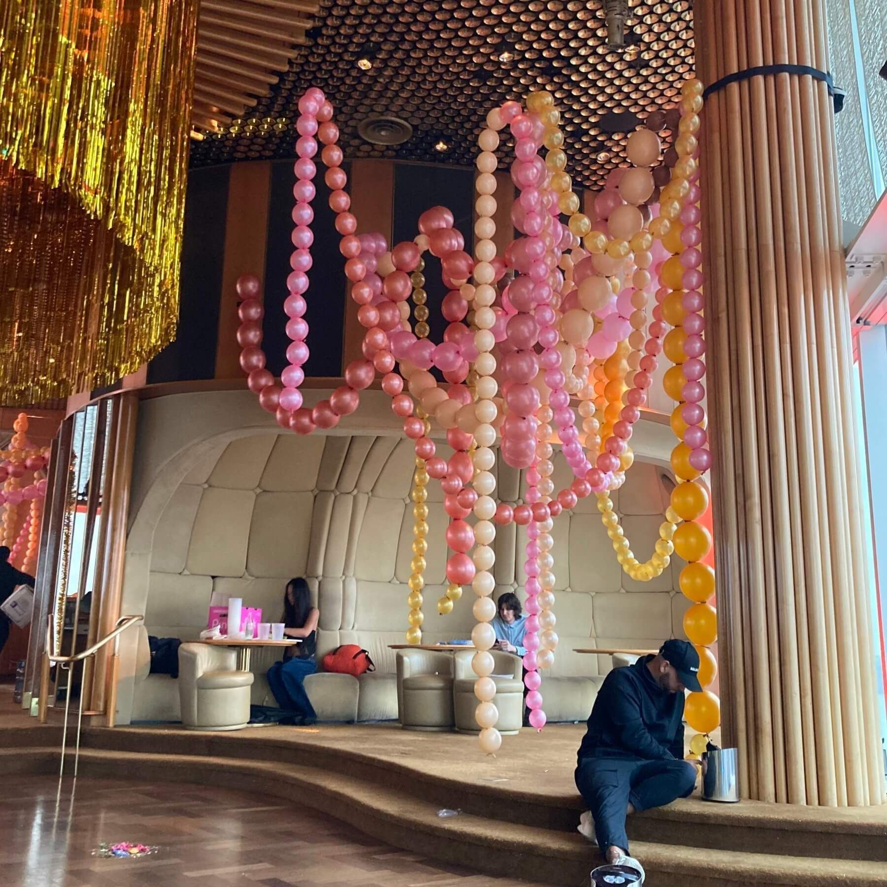 Restaurant interior with balloon garlands. People seated at tables, and by a textured wooden column.
