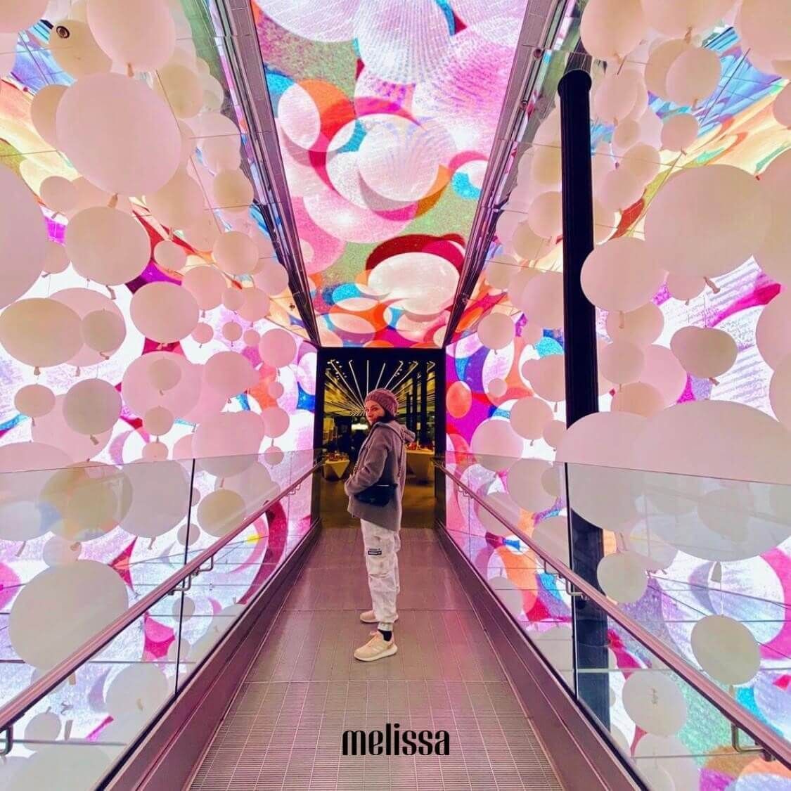 Person in a colorful art installation with pink and white balloon-like shapes.