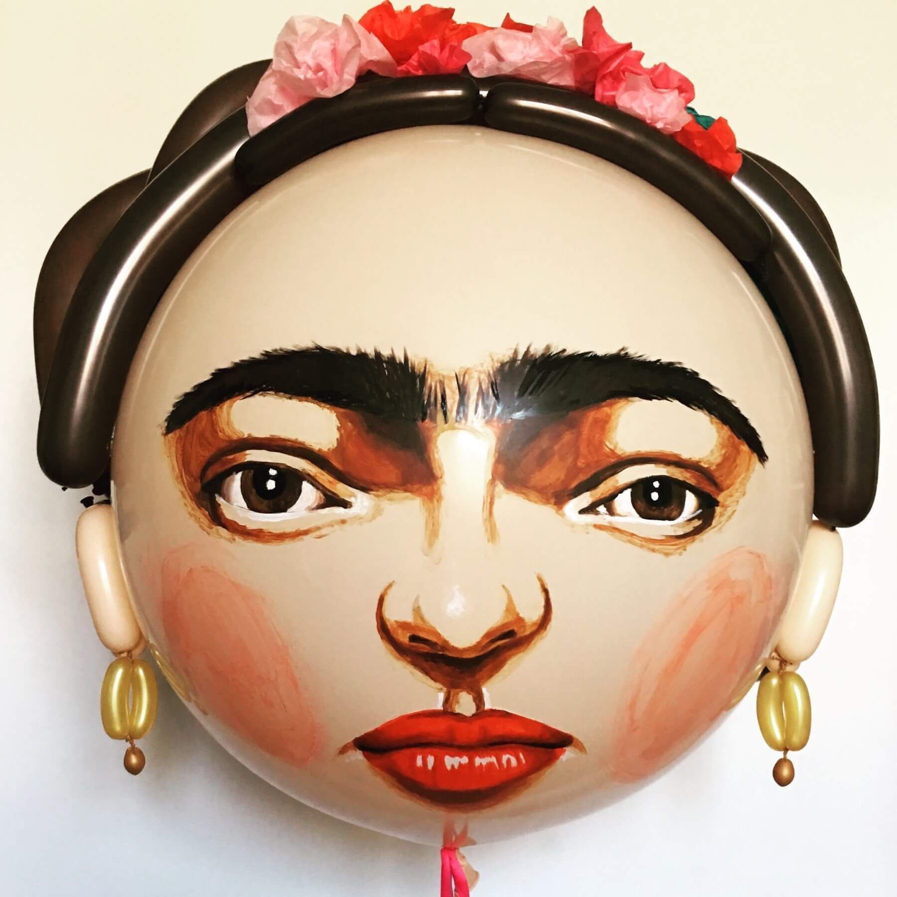 Frida Kahlo balloon with painted features, dark hair, flower crown, and dangling earrings.