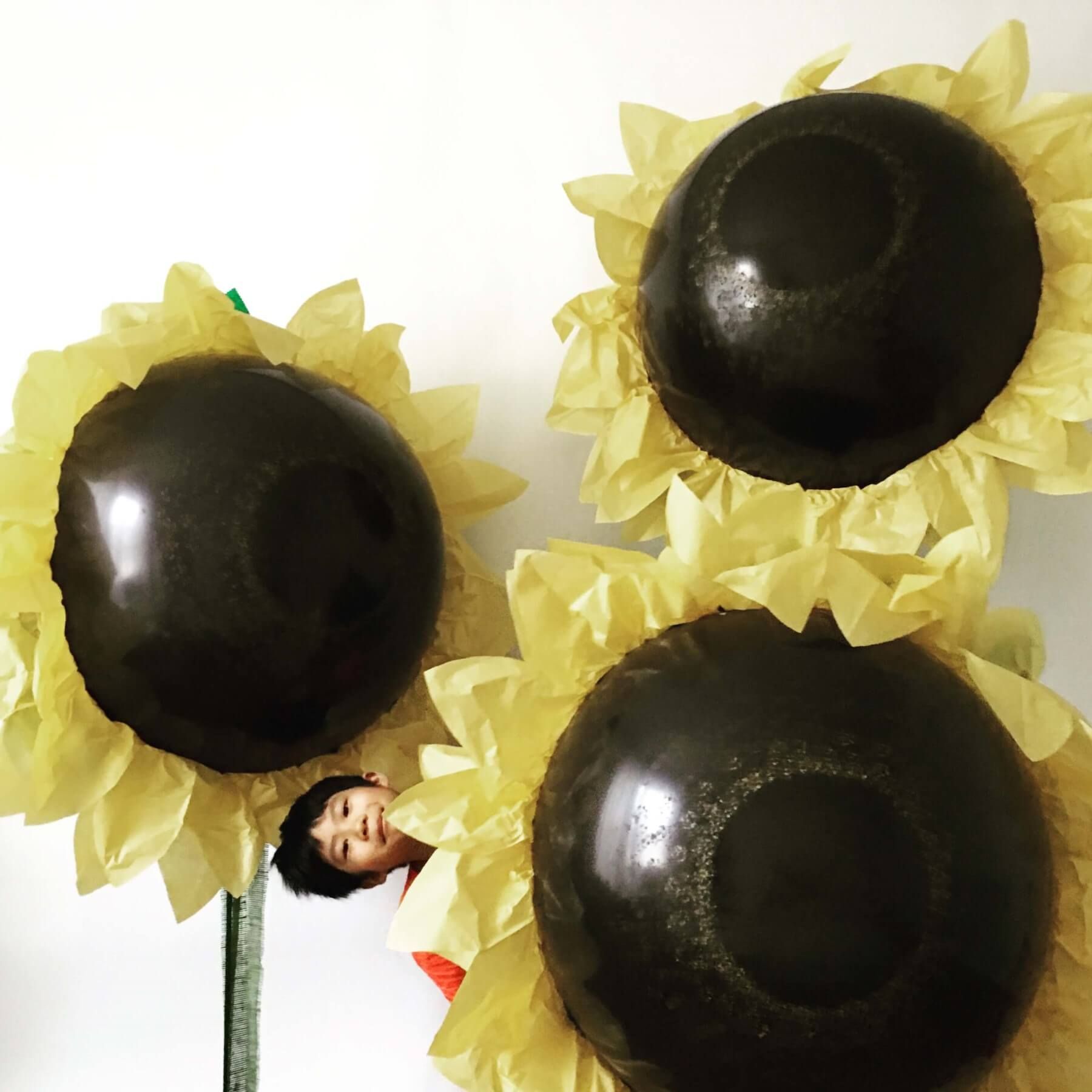 Child peeks out from behind large, paper sunflower decoration.