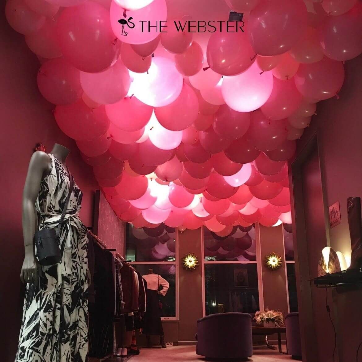 Pink balloons fill the ceiling of a retail space; a mannequin in a dress stands nearby.