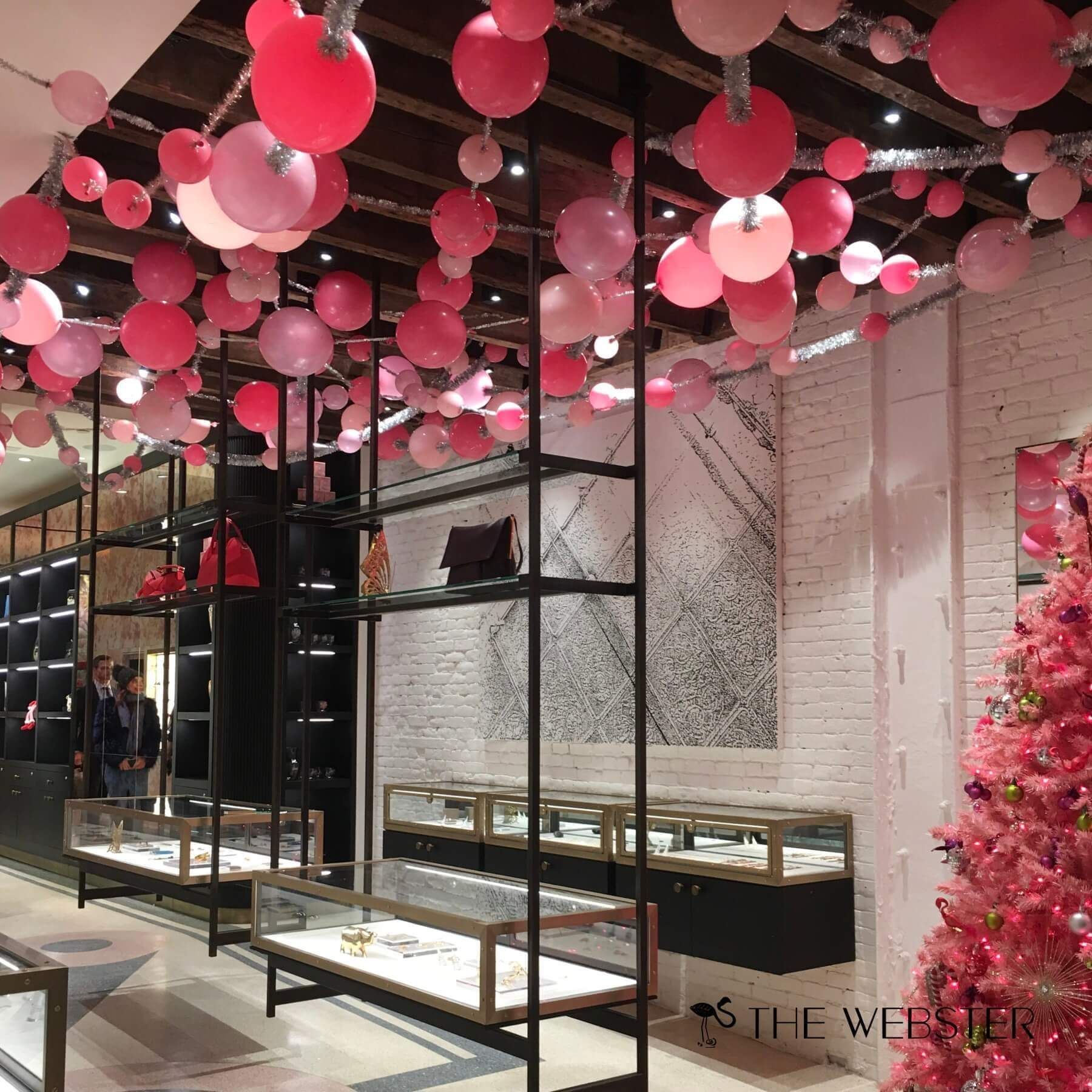 Interior of a store decorated with pink balloons, shelves with items, and a pink Christmas tree.