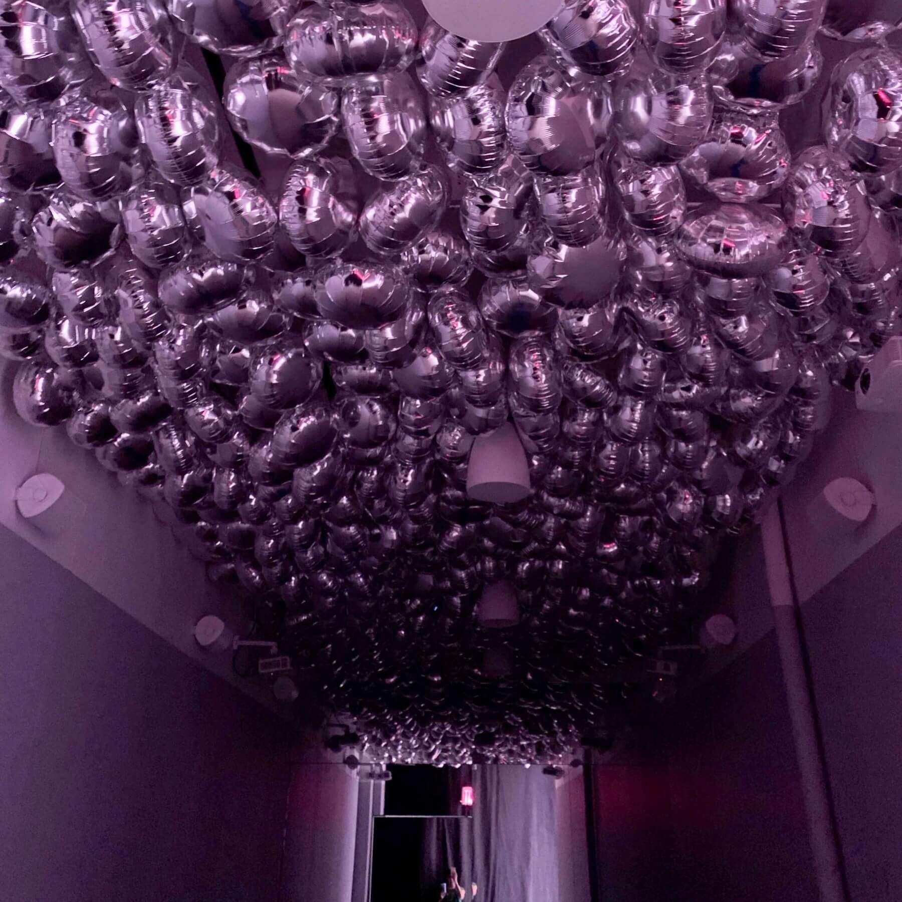 Ceiling installation with many reflective silver orbs filling a corridor, reflecting light.