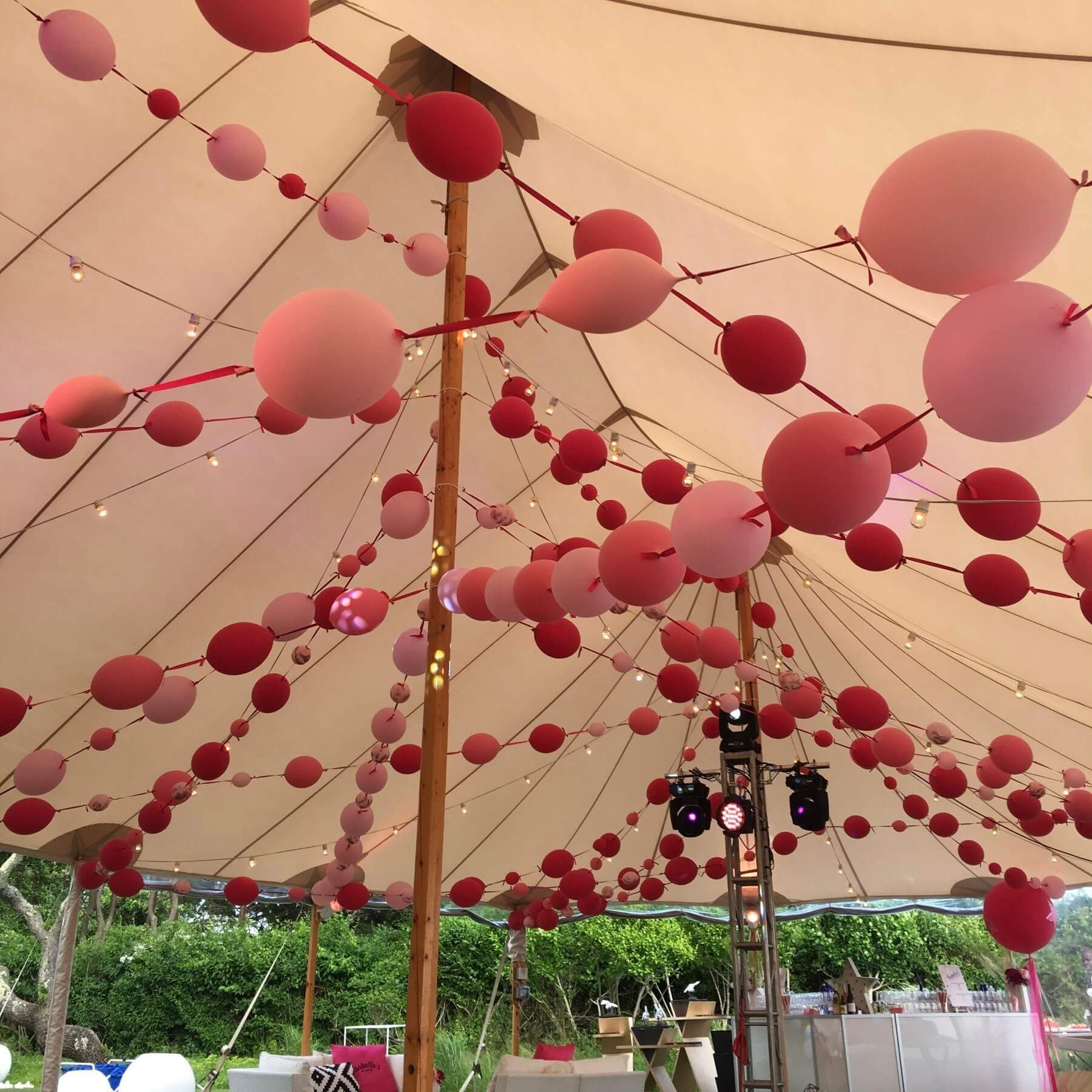 Pink and red balloon garland decorates the interior of a large tent.