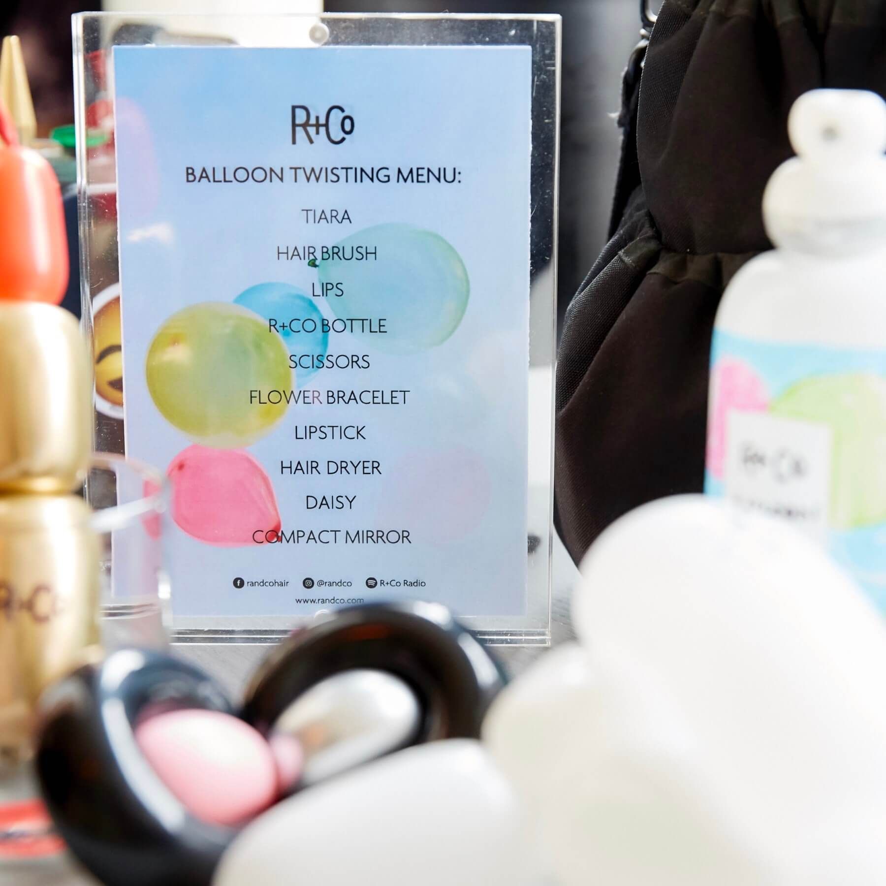 A menu for balloon twisting, with balloons and other objects in foreground, blue and pink background.