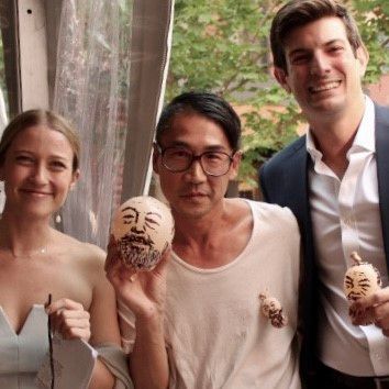 Three people holding decorated gourds, smiling. Outdoor setting.