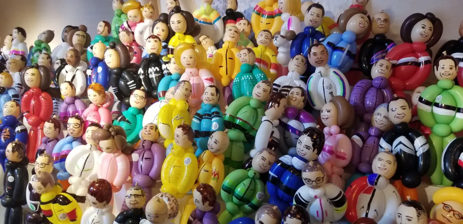 A large group of balloon people are tightly clustered together, each with a wooden head and colorful balloon bodies.