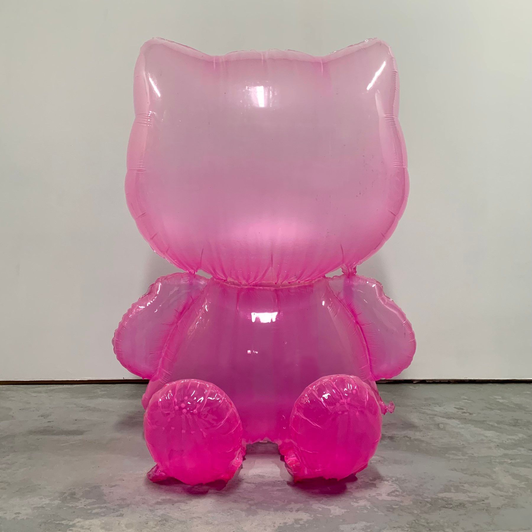 A pink hello kitty balloon is sitting on a concrete floor.