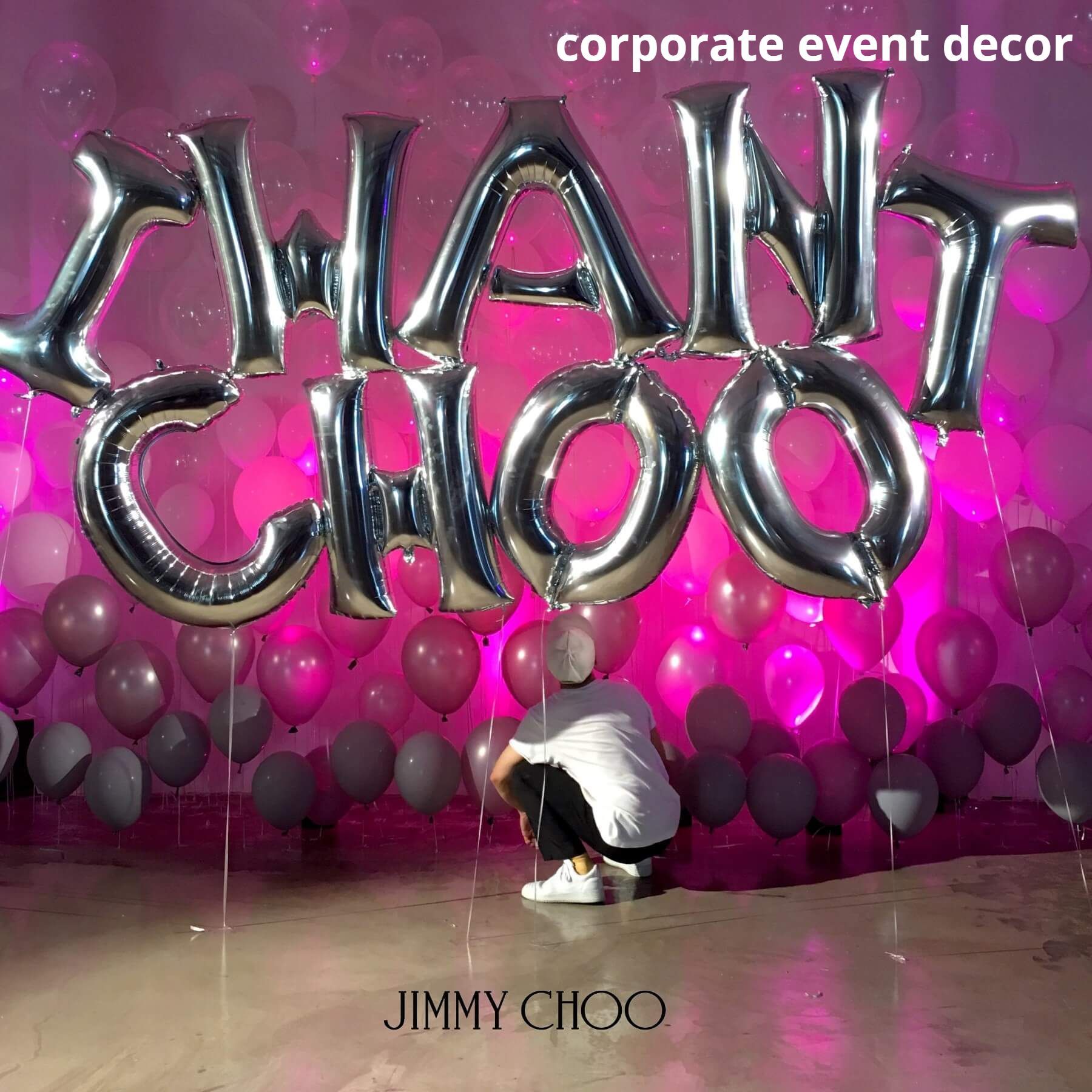 A man is kneeling in front of a wall of balloons that say jimmy choo