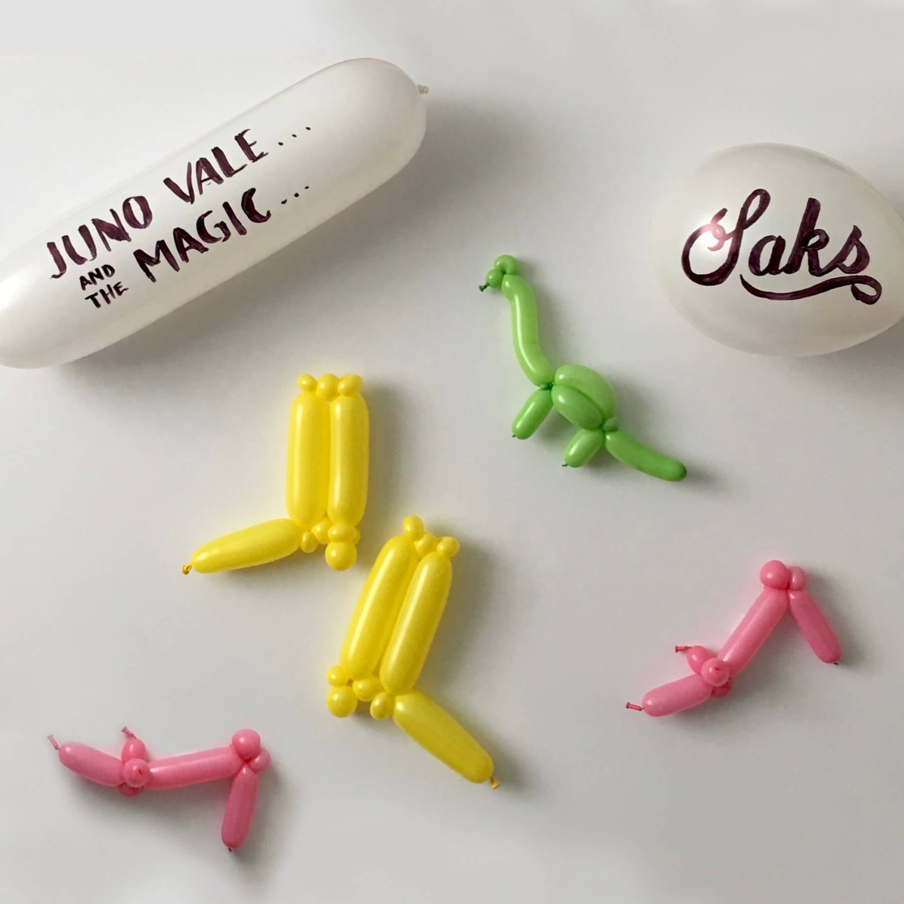 White balloons with text and balloon animals in yellow, green, and pink colors.