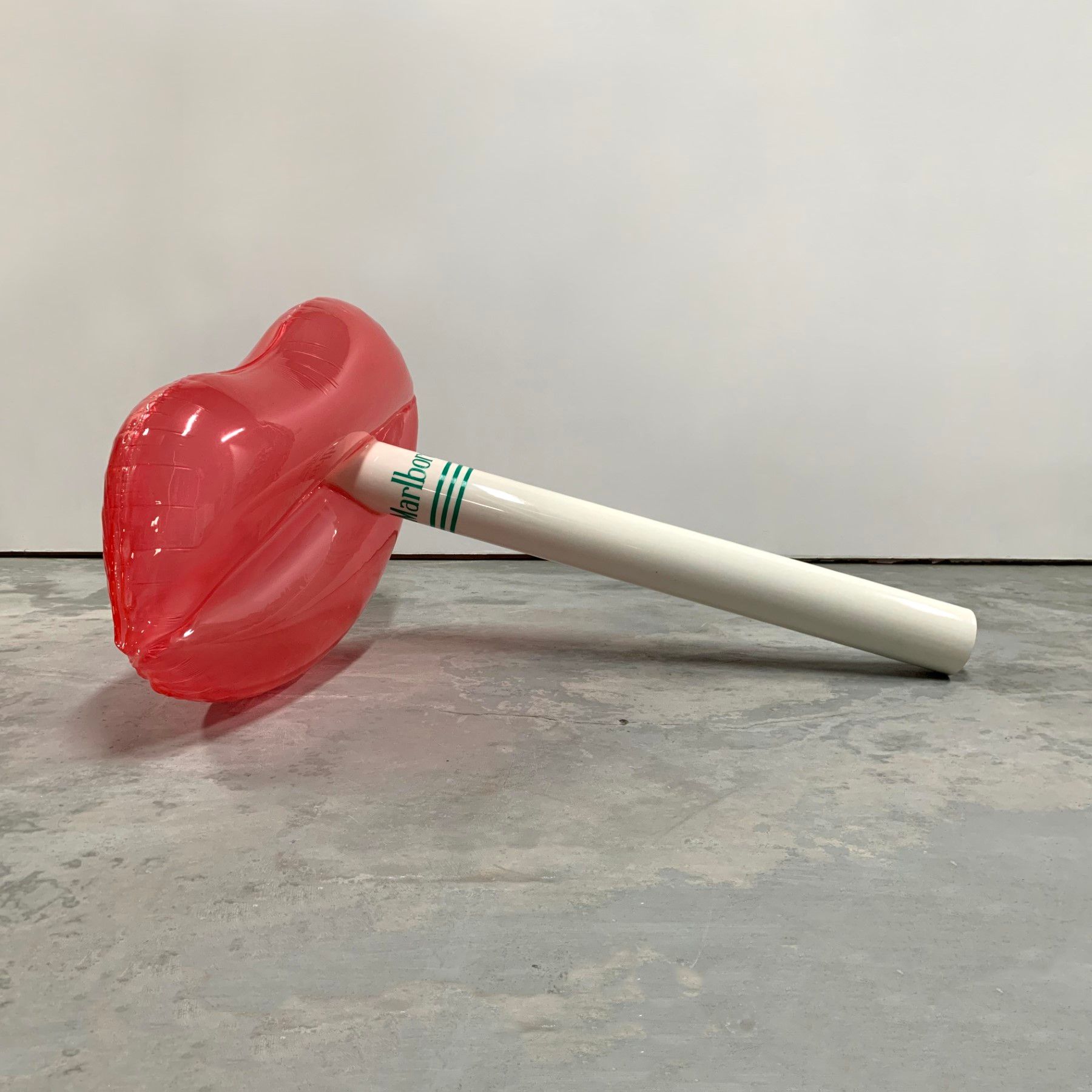 A red lollipop with a white stick is sitting on a concrete floor.