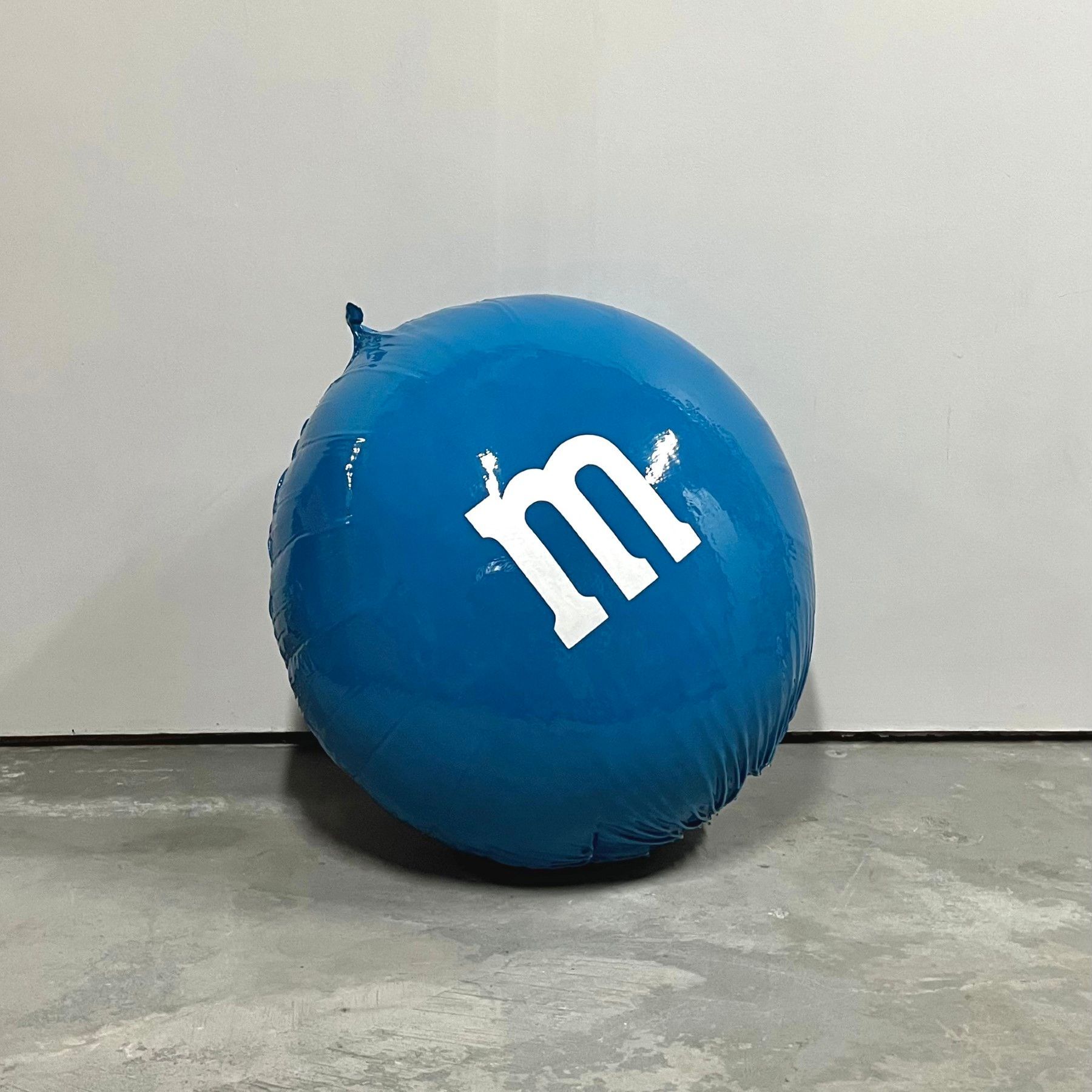 A blue m & m balloon is sitting on a concrete floor