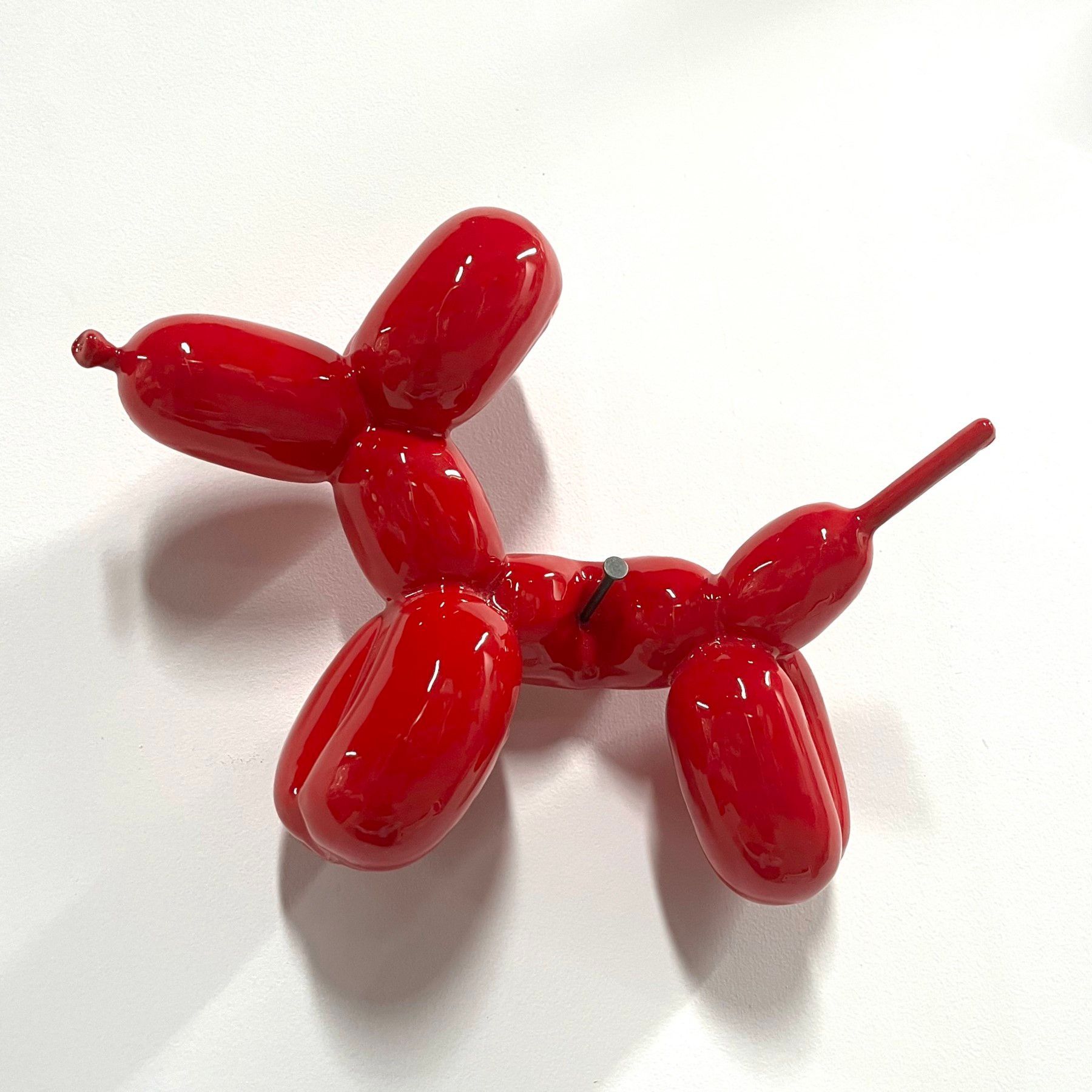 A red balloon dog is sitting on a white surface