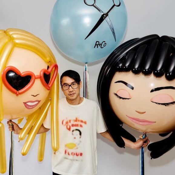 A man stands next to two balloons one of which says r & co
