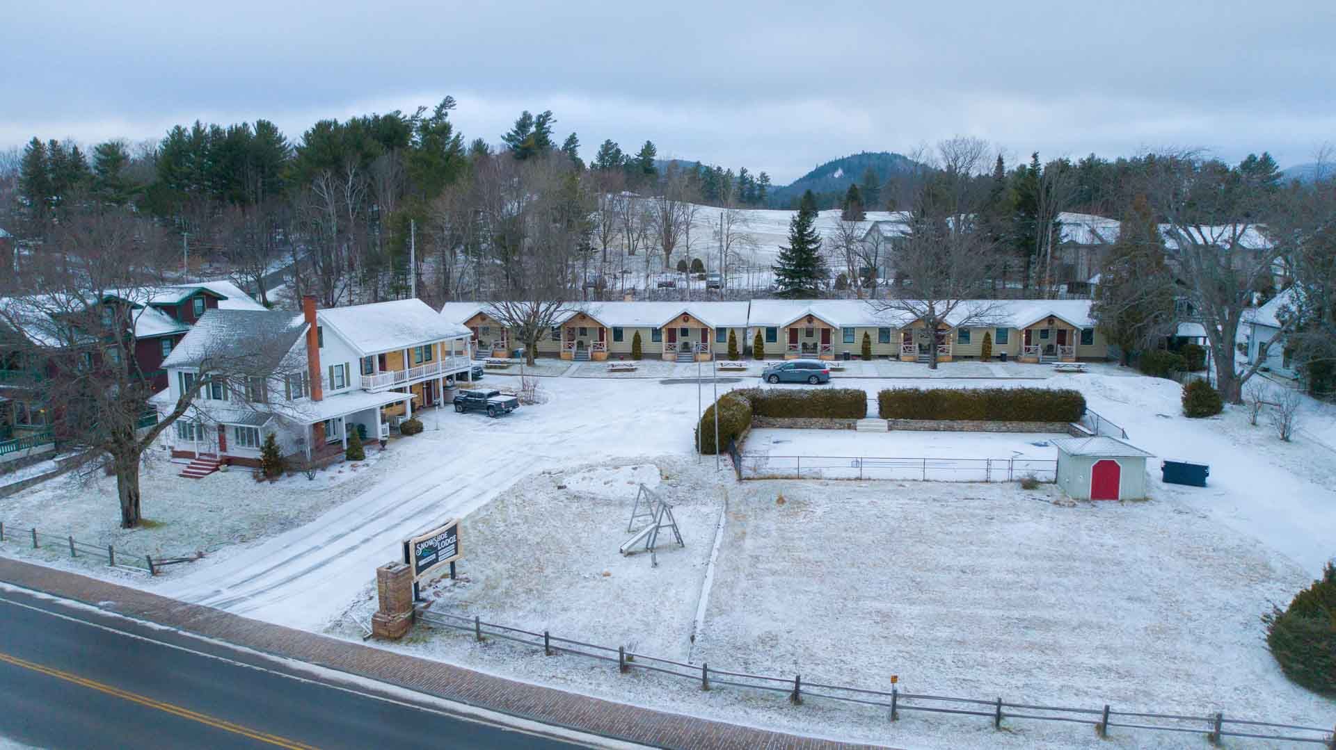 An aerial view of a snow covered field with houses and trees in the background.