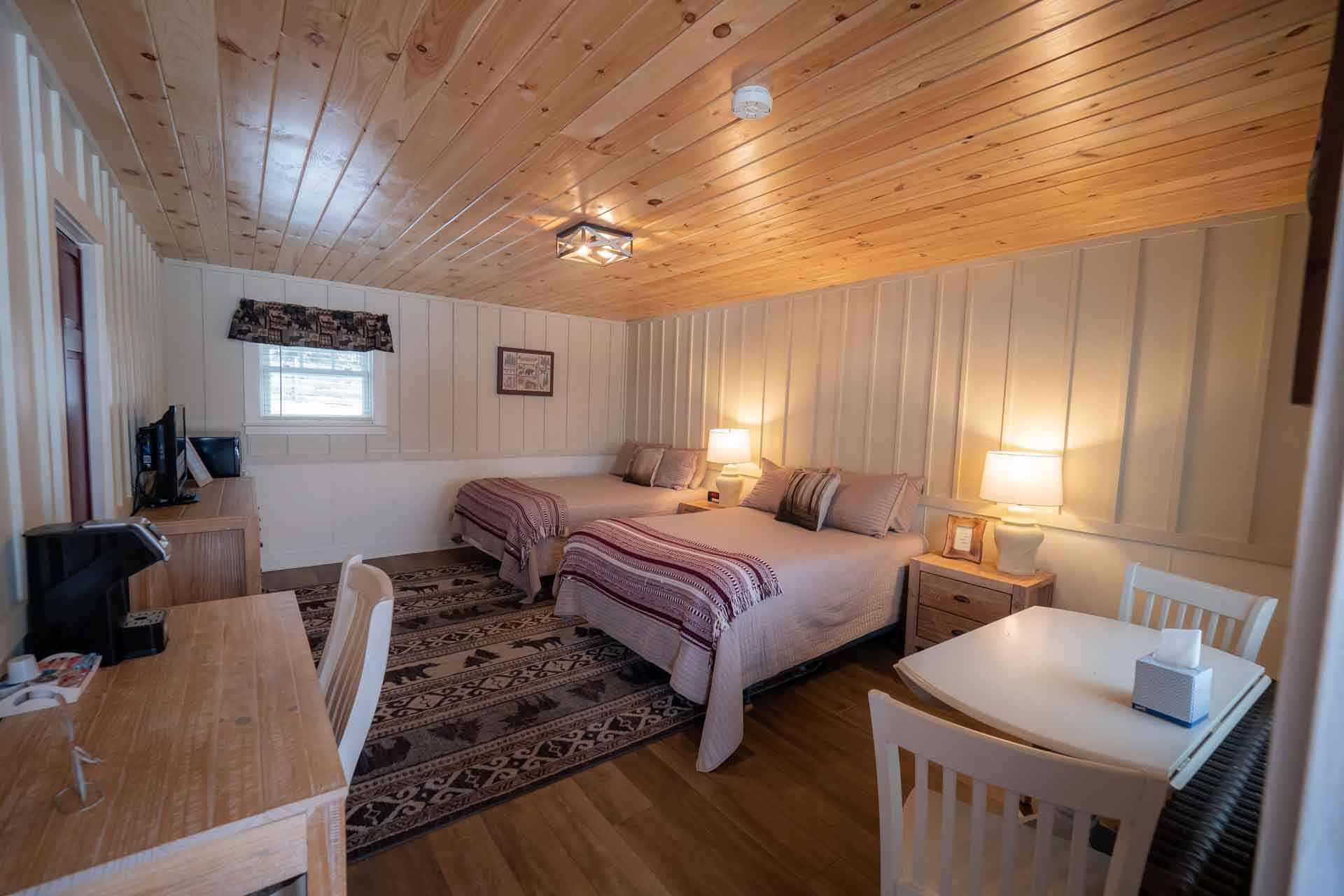 A hotel room with two beds, a table, and chairs.