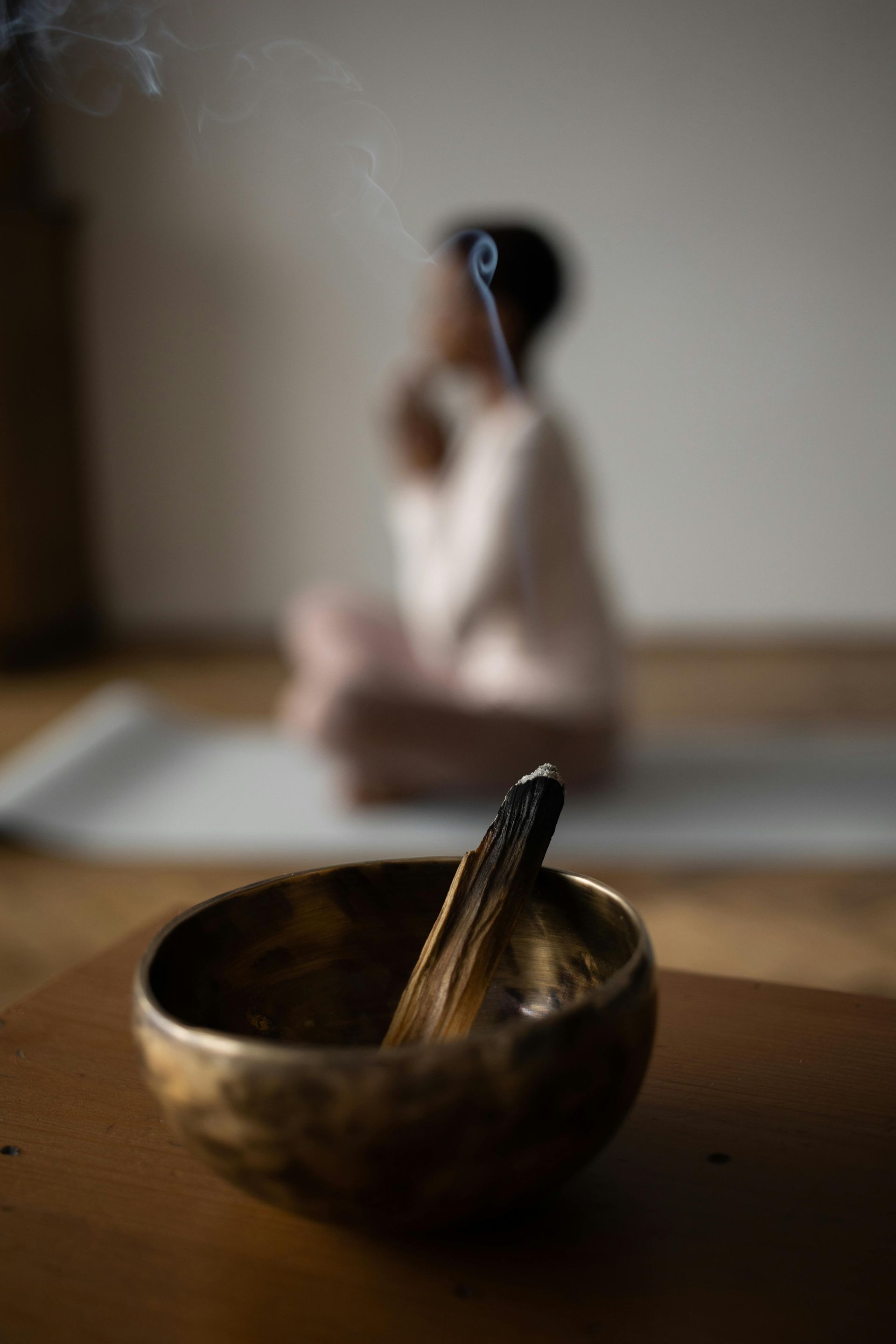 Woman meditating on a mat in a dim room, with a singing bowl in the foreground.