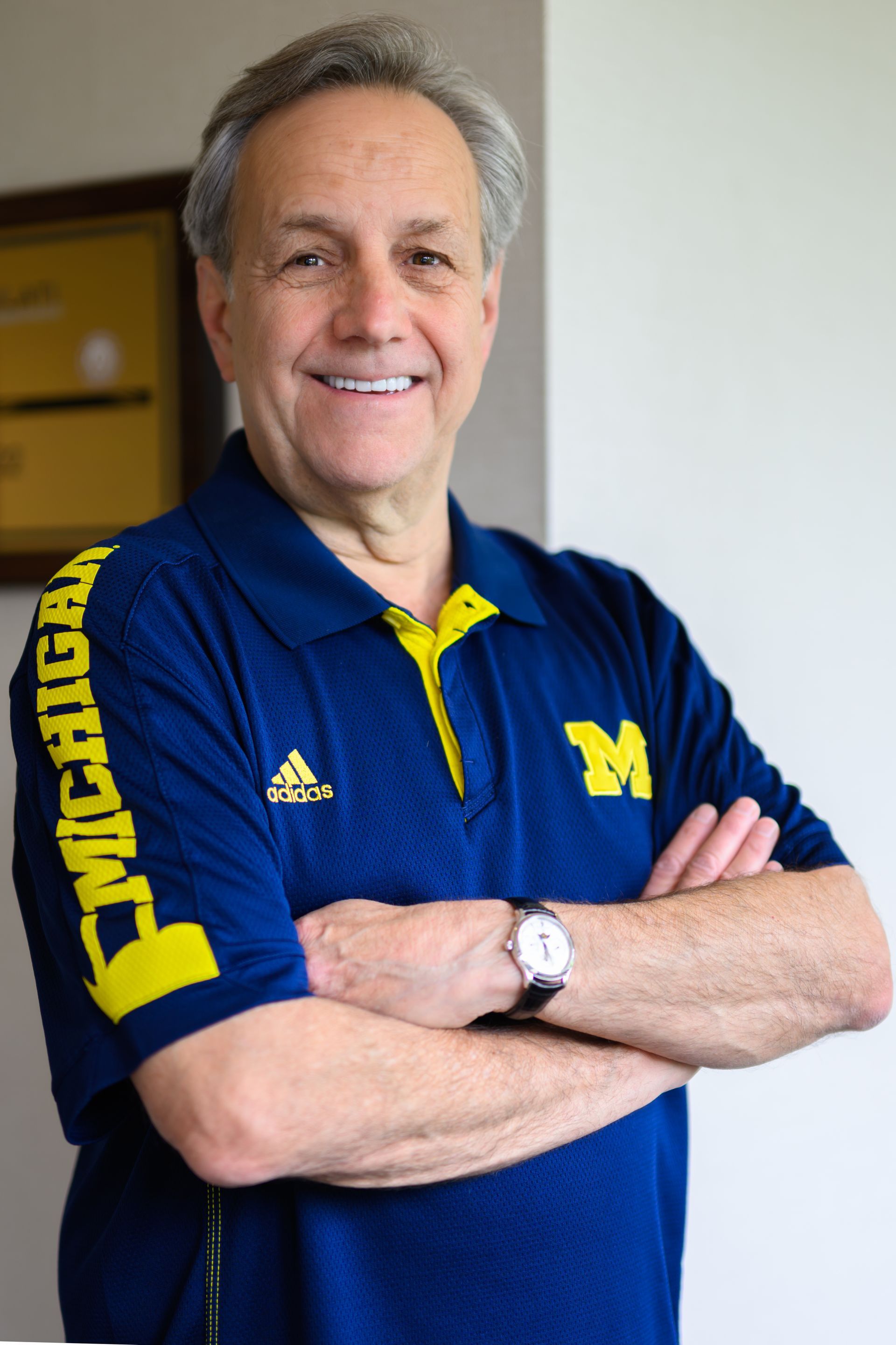 Man with arms crossed, wearing a blue Michigan polo shirt, smiling.
