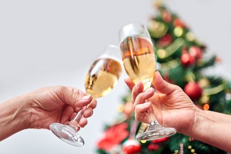 Dos personas brindan con copas de champán frente a un árbol de Navidad.