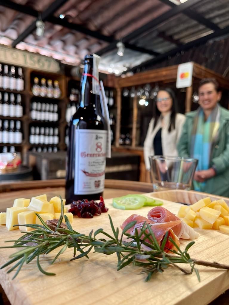Una botella de vino se encuentra encima de una tabla de cortar de madera con queso y carne.