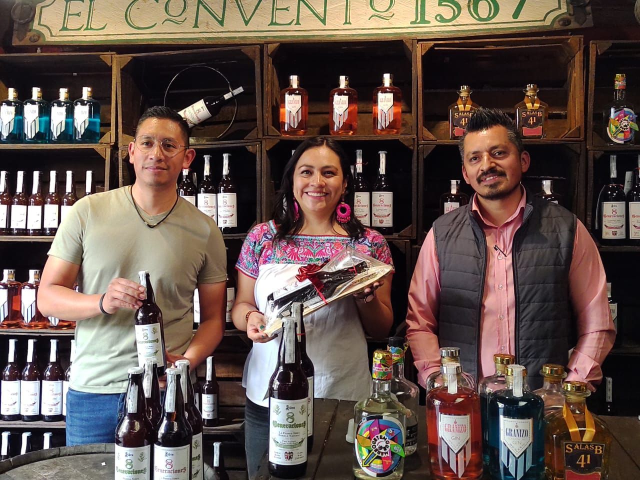 Tres personas están de pie delante de una exposición de botellas de vino.
