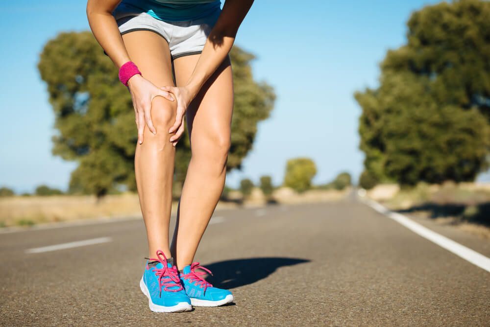A woman is holding her knee in pain while standing on a road.