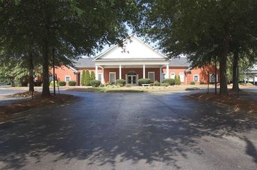 Brick building with white columns, framed by trees and a wide driveway in front