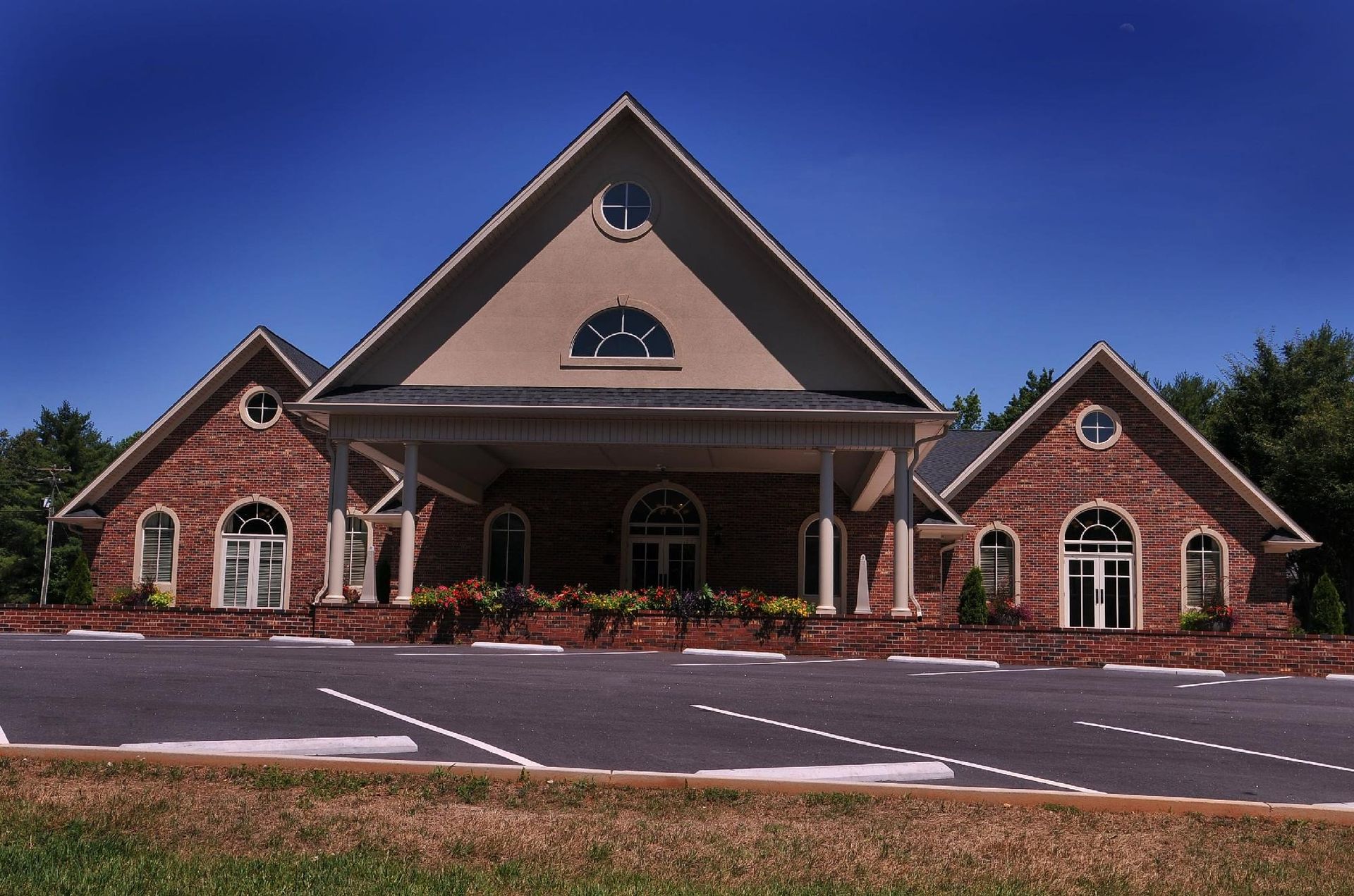 Brick church building with a covered entrance, arched windows, and a peaked roof under a clear blue sky