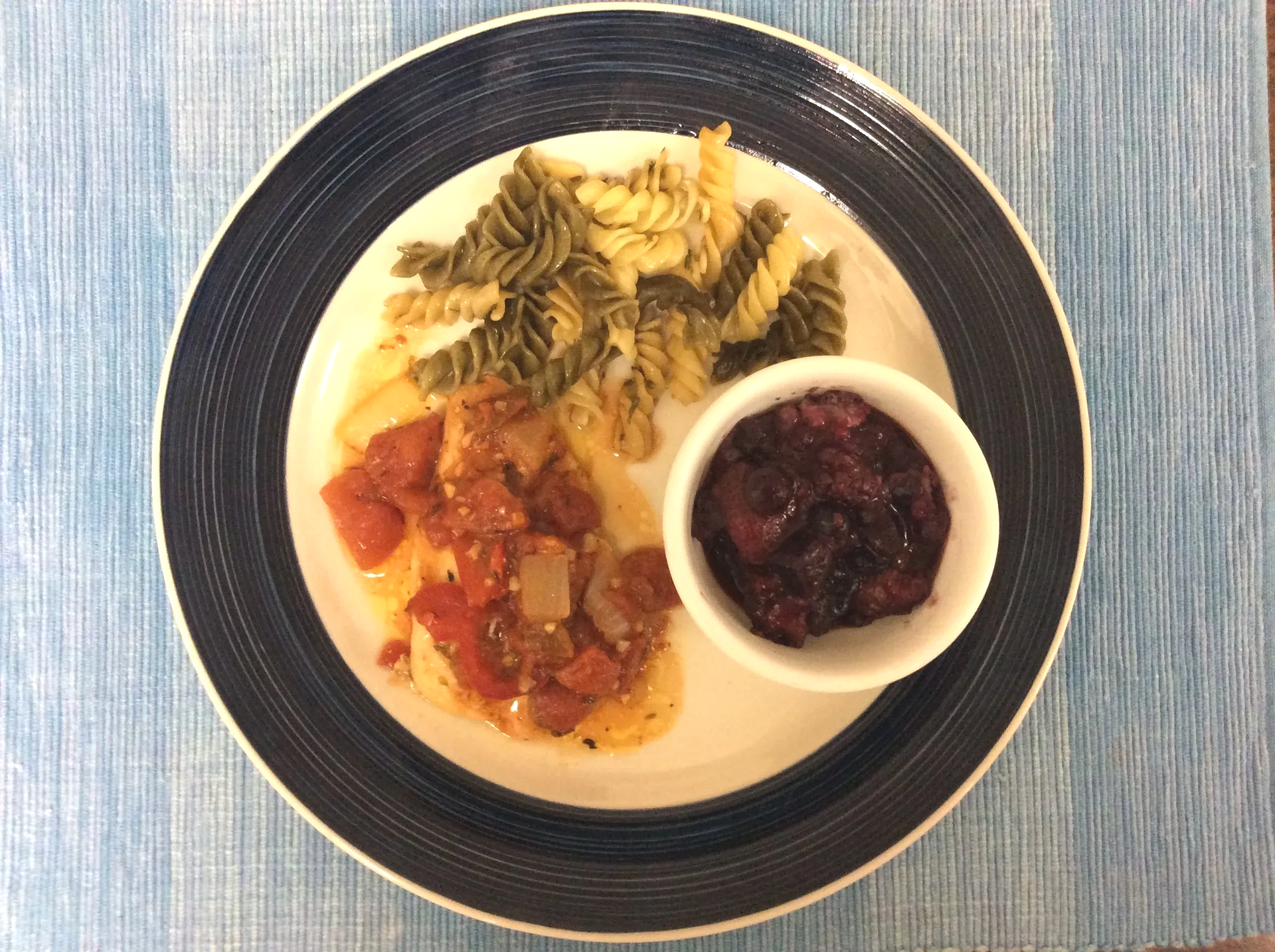Overhead view of a plated meal with pasta, sauce, and a small bowl of dark fruit compote