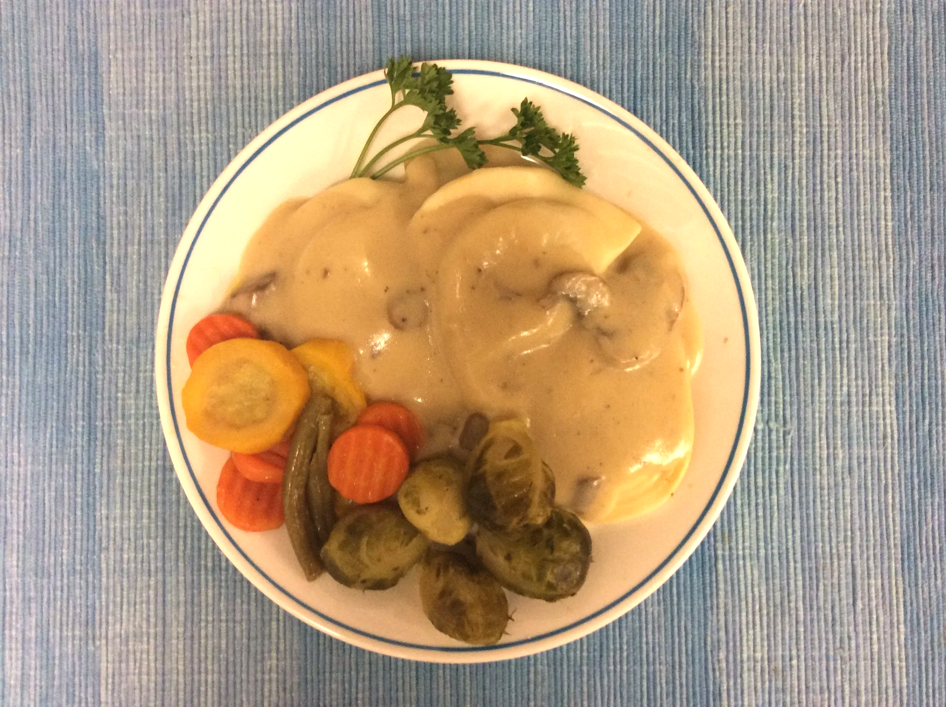 Plate of chicken in creamy sauce with roasted vegetables on a blue tablecloth